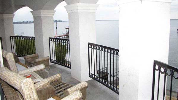 Covered balcony with arched openings, decorative railing, and seating overlooking water.