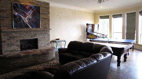 Recreation room with stone fireplace, billiards table, pinball machine, and large windows.