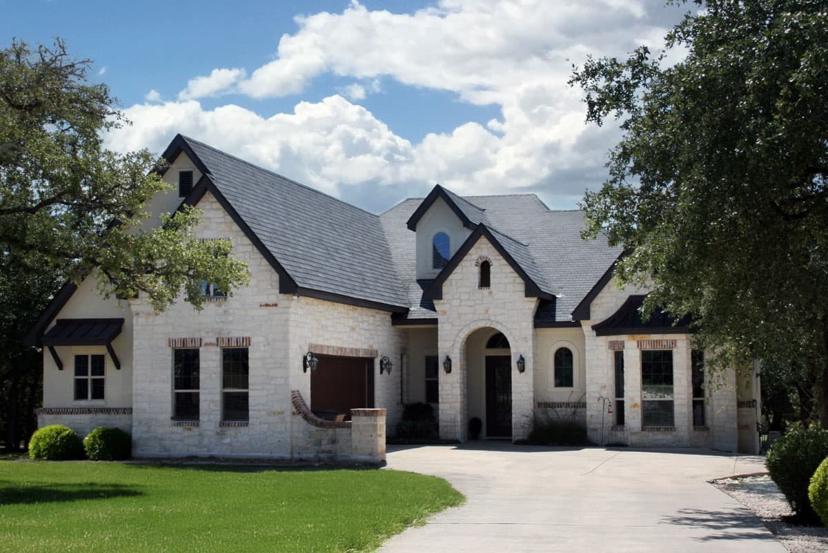 House plan exterior. Two-story home in a French Country style, featuring arched entryway, multiple gables, and a stone facade. Dark roof and accents.