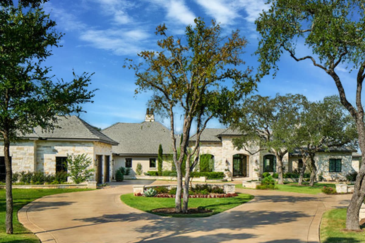 House plan exterior. Stone facade, multiple gabled roofs, and an arched entry. Features include a circular driveway and manicured landscaping.