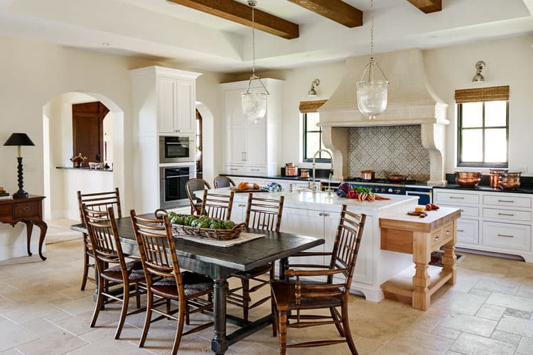 Kitchen with central island, range hood with tile backsplash, dining table, and exposed wood ceiling beams.