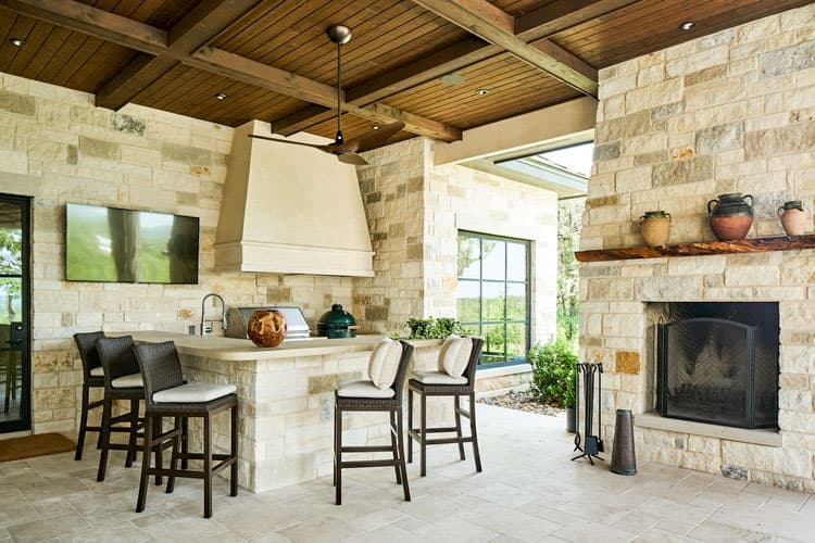 Covered outdoor patio with stone fireplace, built-in bar with grill, and wood-beamed ceiling.