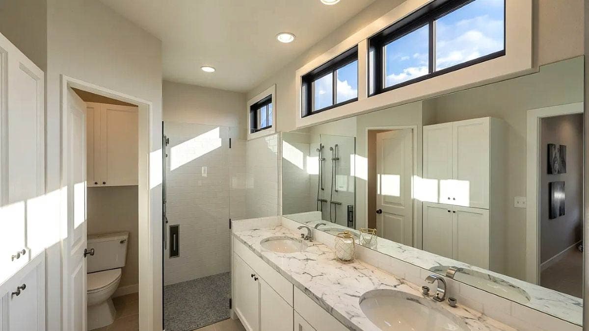 Modern bathroom with dual vanity, marble countertop, glass-enclosed shower, and private toilet area.
