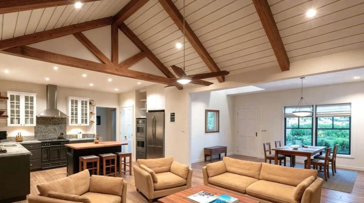 Open-plan living area with kitchen, dining, and seating. Features vaulted ceiling with exposed wood beams, kitchen island, and large windows.