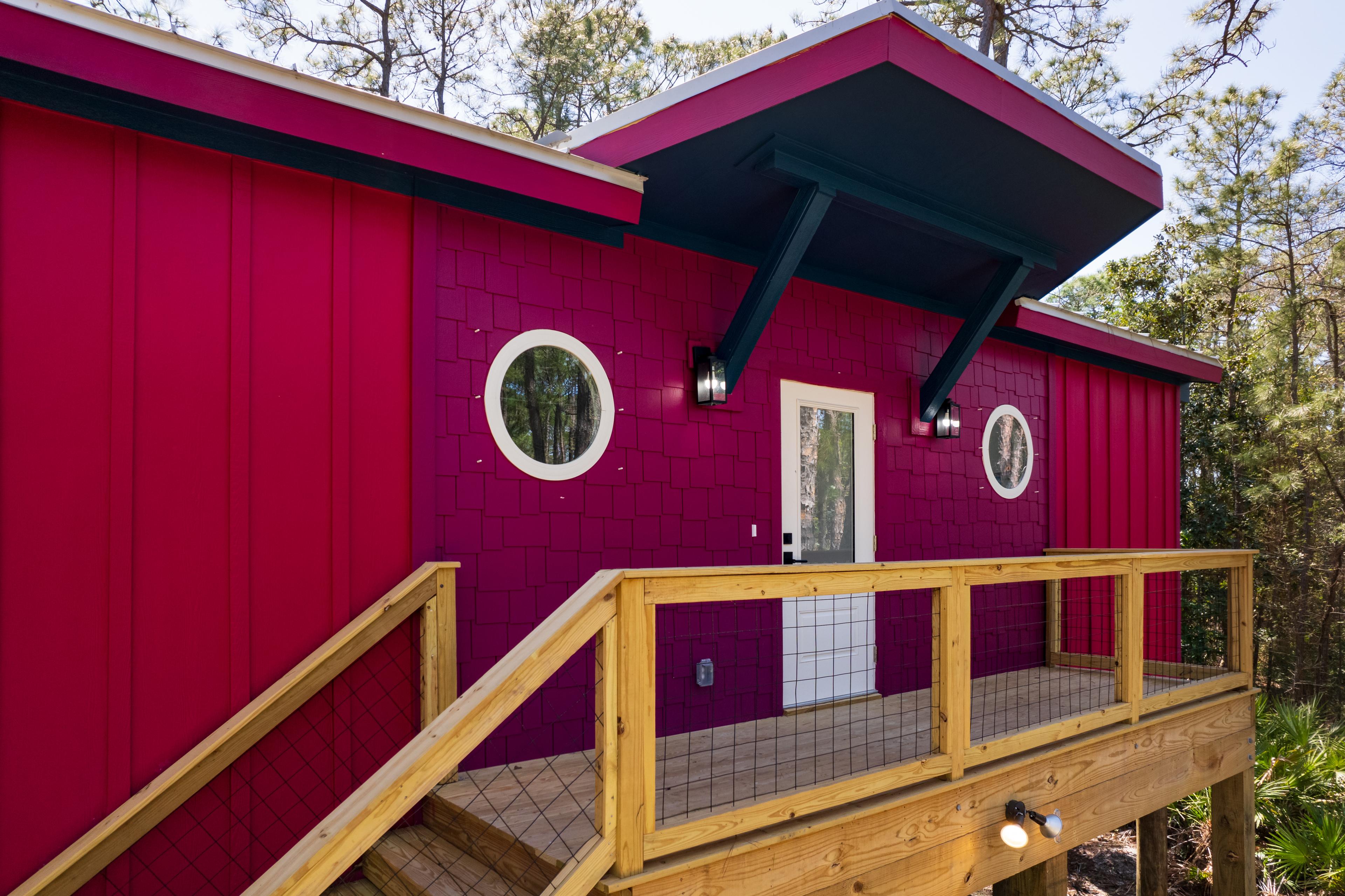 House plan exterior: red siding, wood deck with wire railing, porch light, and circular window.
