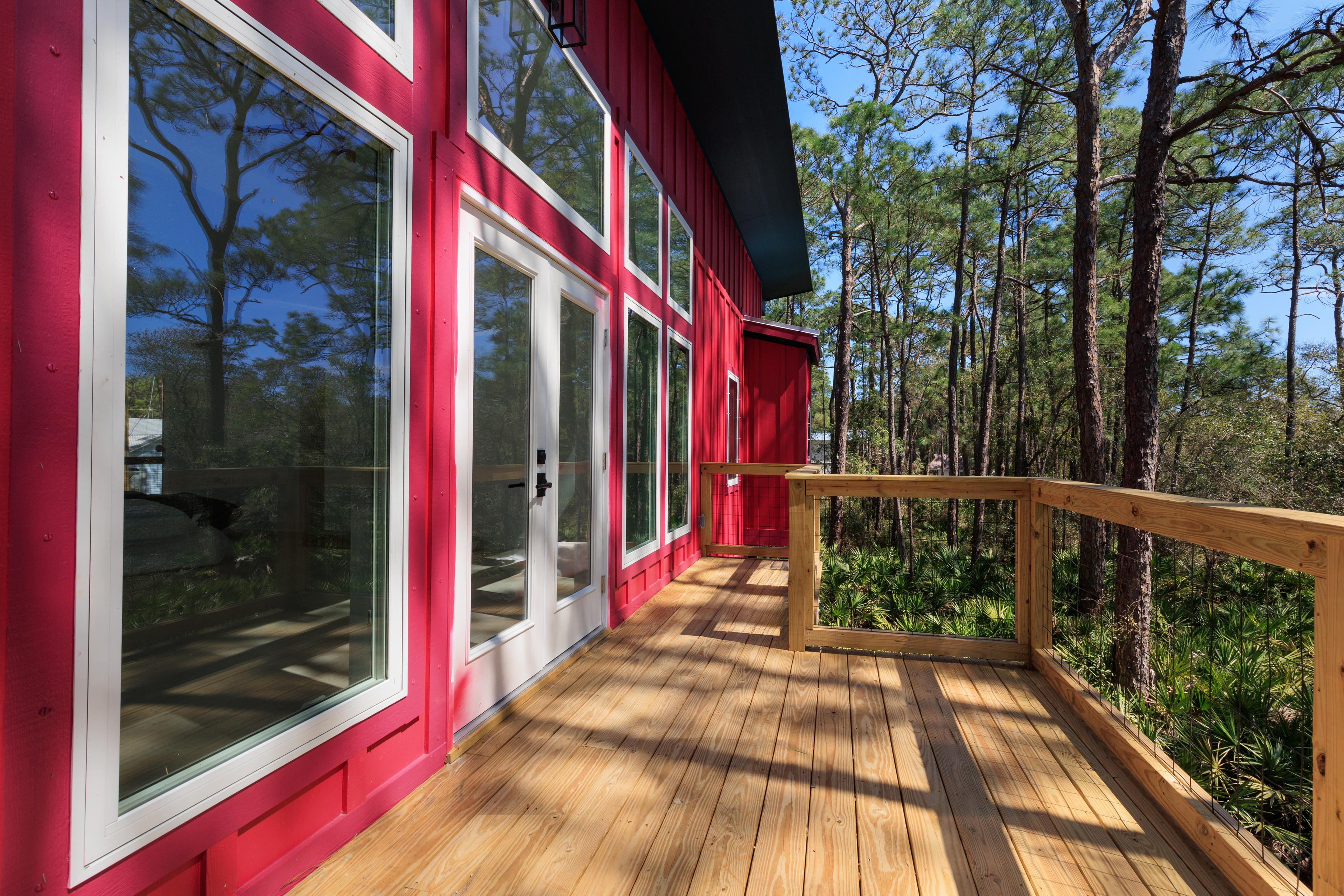 House plan exterior with red siding, multiple large windows, glass double doors, and a wooden deck and railing.