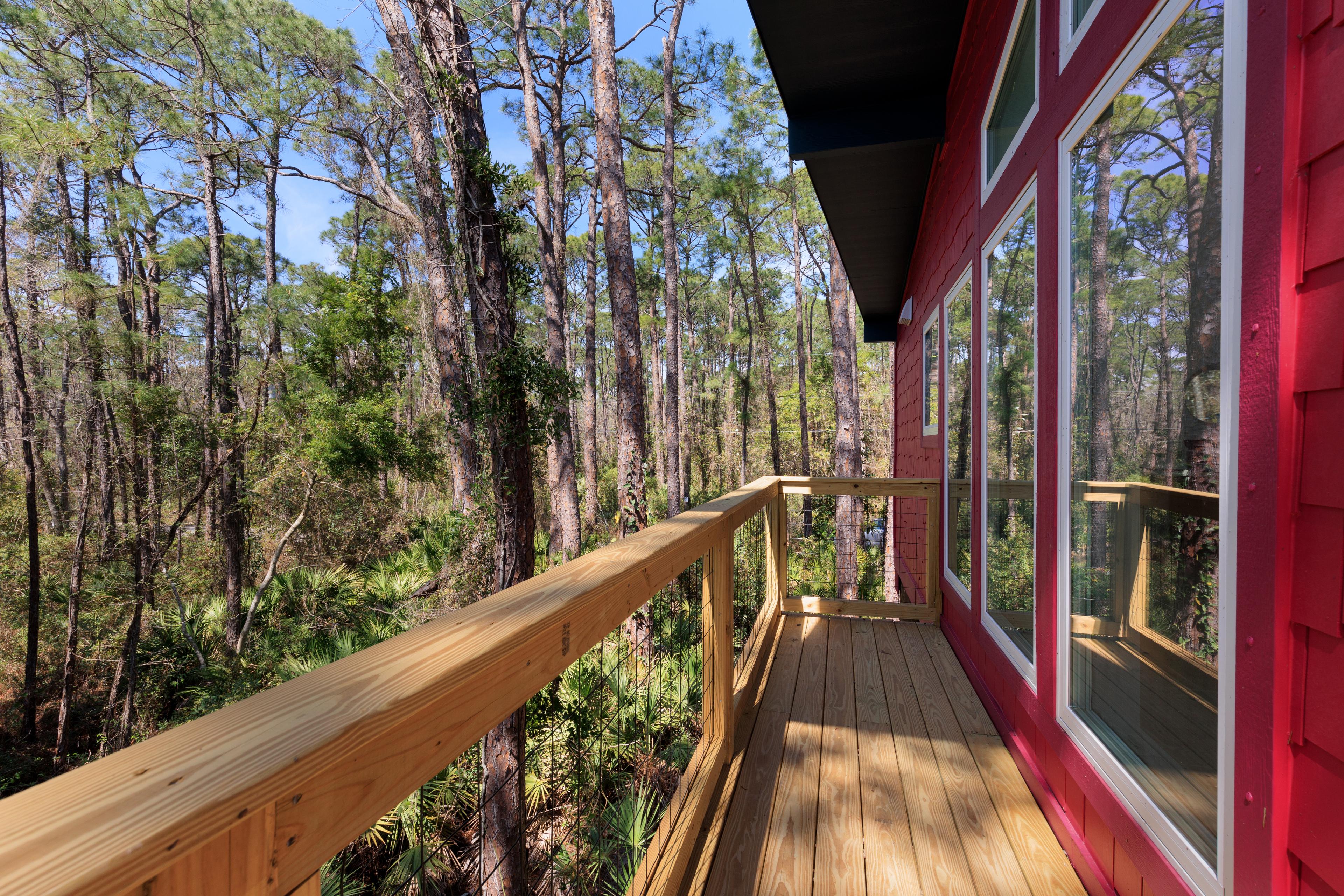 House plan exterior with wooden deck, red siding, and large windows overlooking a forest.