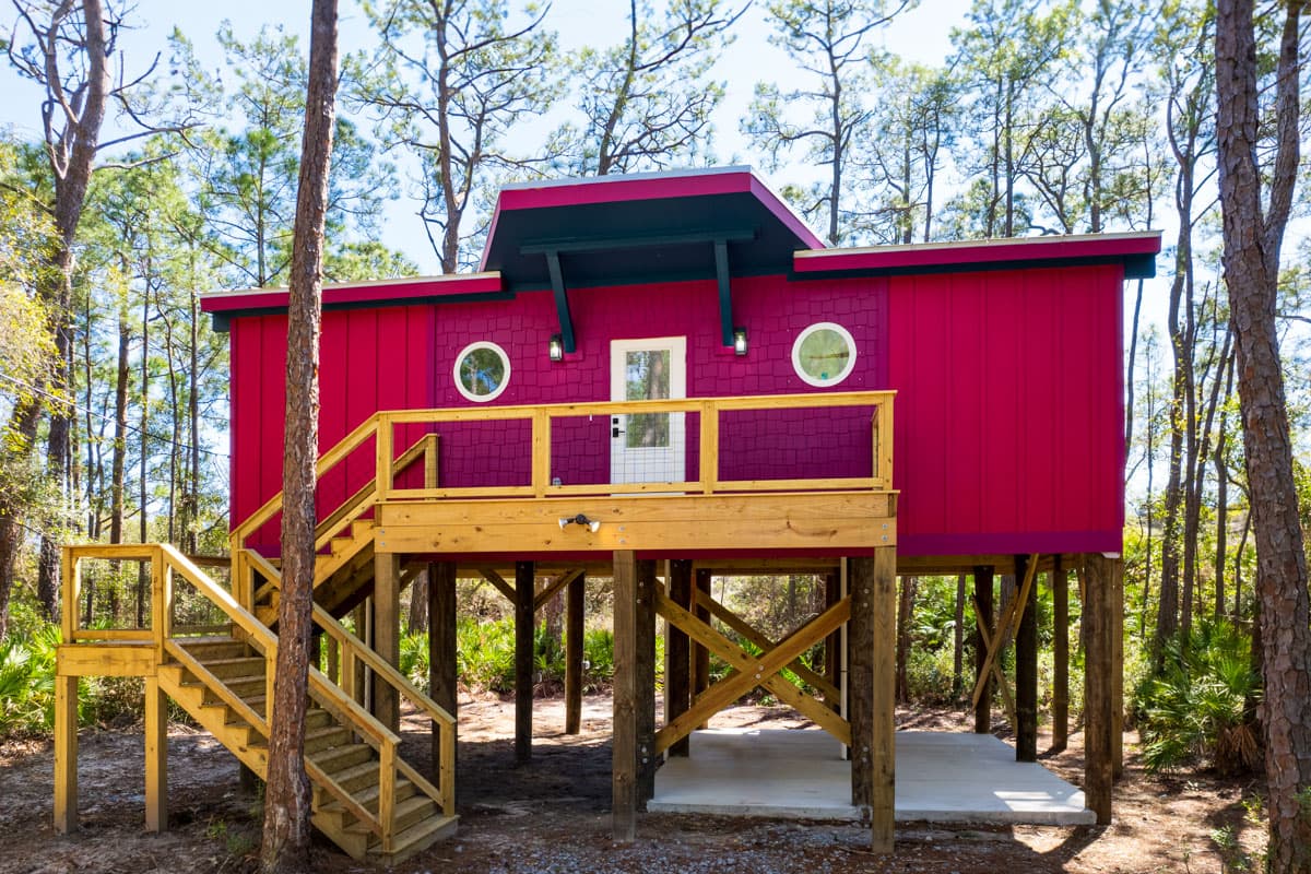 House plan exterior. One-story structure with elevated platform. Features include a front porch, round windows, and an angled roofline.
