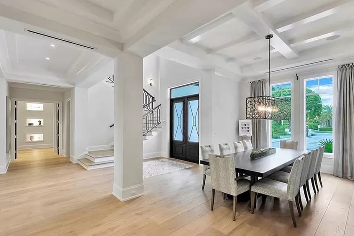 Interior view of an open-concept dining room with coffered ceiling, staircase, and double entry doors.