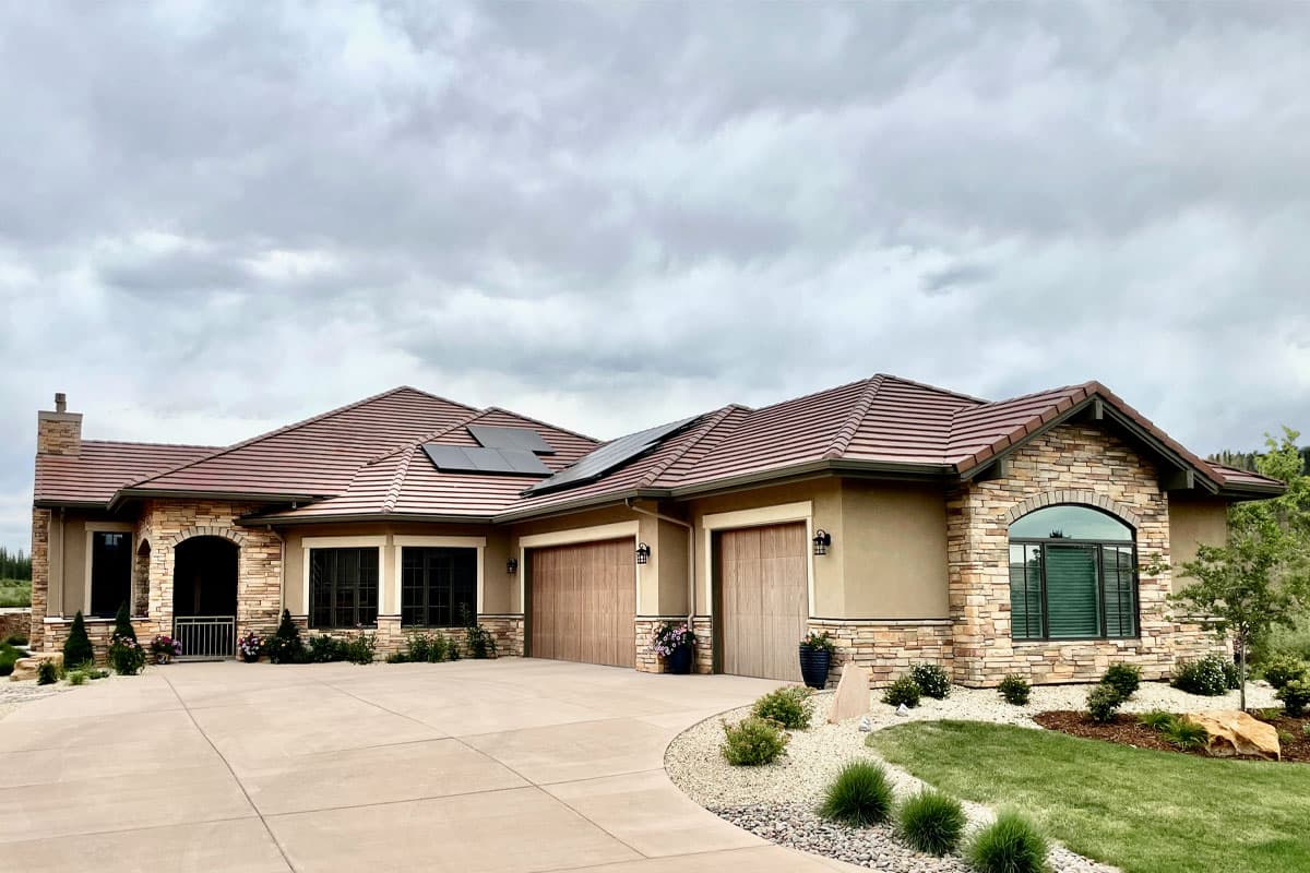 House plan exterior. One-story house with stone accents, arched entryway, and attached garage. Features include tiled roof and dormers.