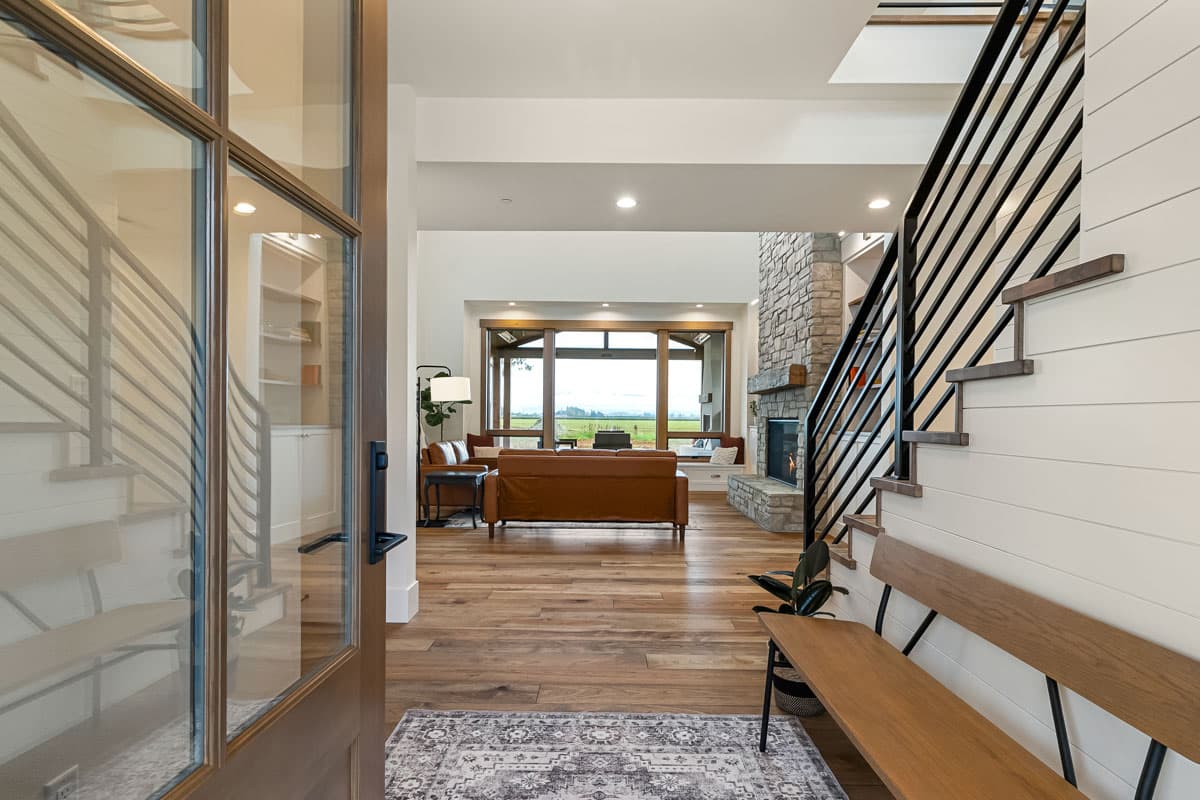 Interior view of a living room with a stone fireplace, leather sofas, and large windows overlooking a field.