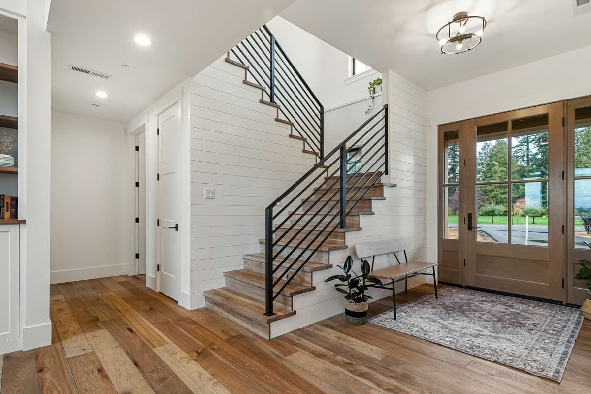 Interior view: Entryway with wood flooring, shiplap accent wall, open staircase with black railing, and double glass doors.