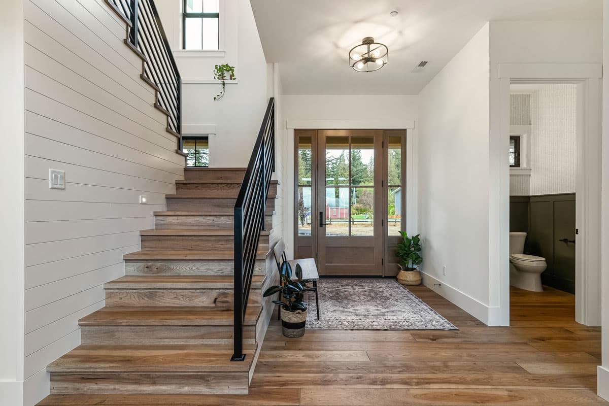 Entryway with wooden stairs, black railings, shiplap wall, double glass doors, and patterned rug.