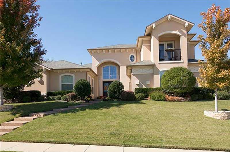 House plan exterior of a two-story home with stucco facade, arched entryway, and second-story balcony.