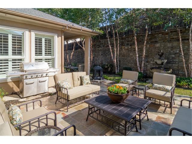 Outdoor living space with built-in grill, covered patio, stone wall fountain, and seating area.