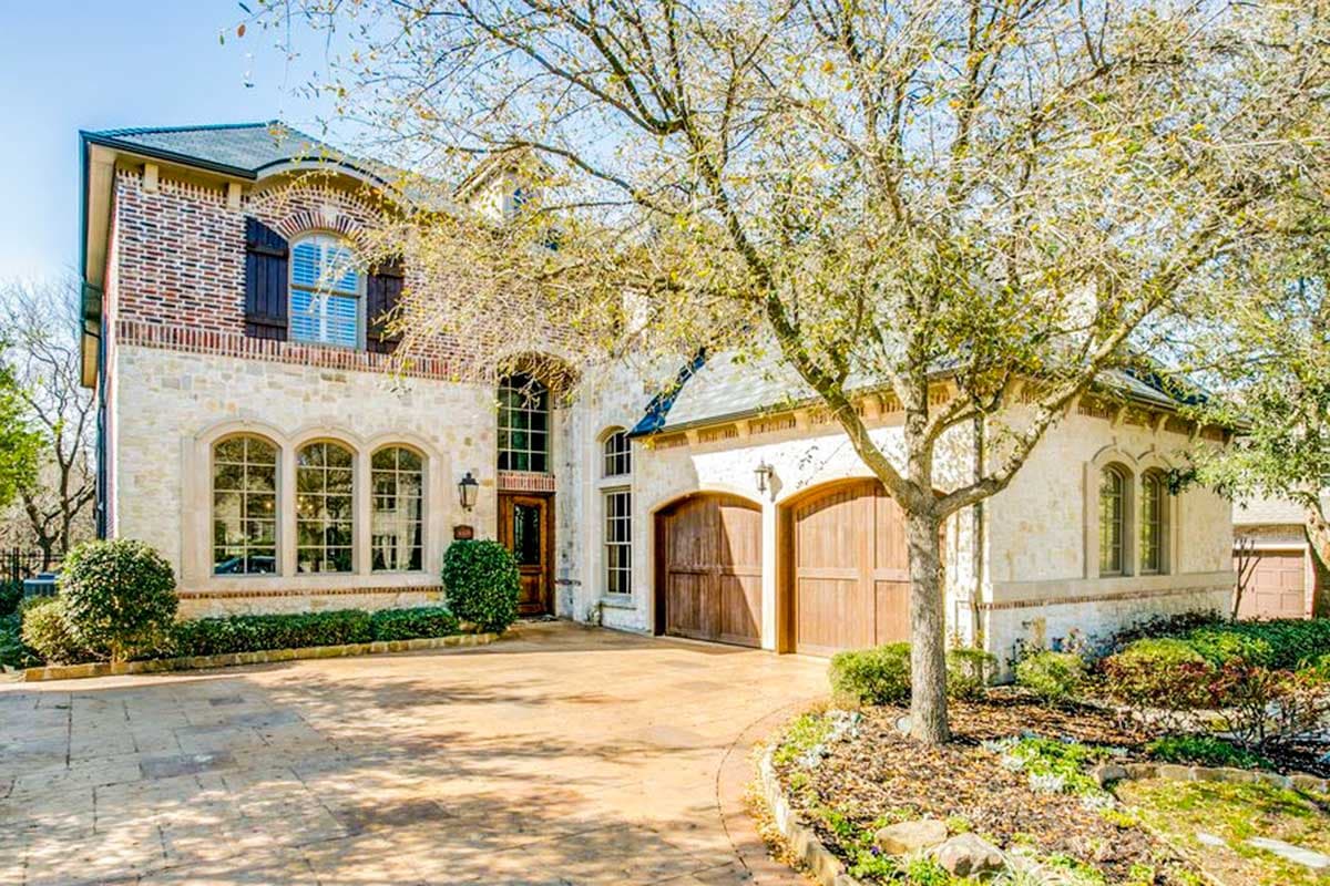 House plan exterior. Two-story house in a French Country style. Features include arched windows, a front-entry garage, and brick accents.