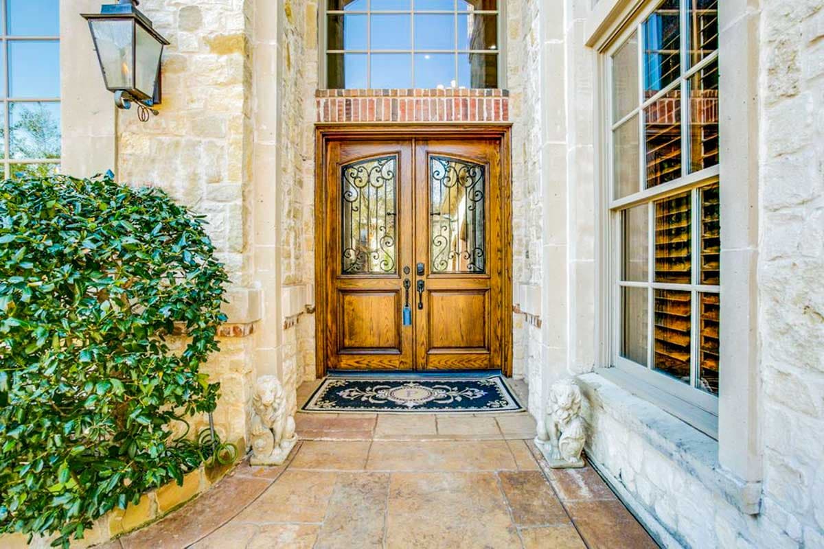 Exterior house plan: Double wooden doors with wrought iron inserts, arched transom window, stone facade, and flanking lion statues.