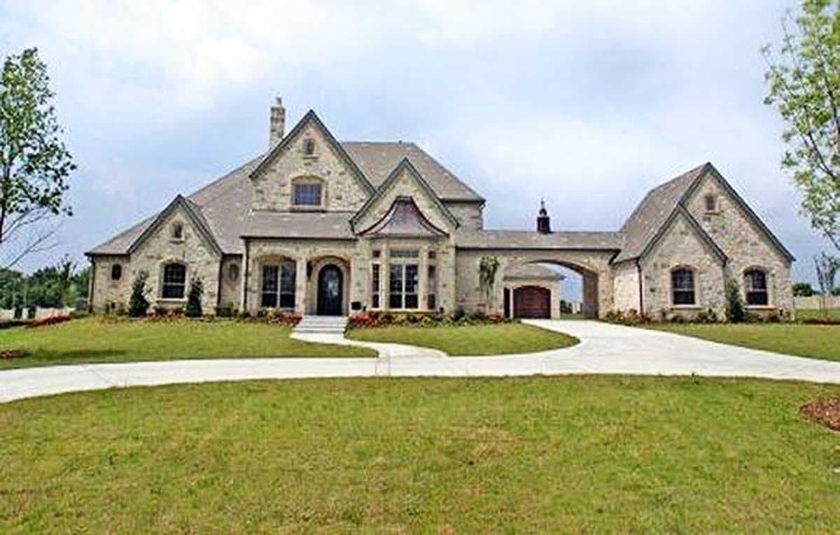 House plan exterior. Two-story, stone-clad house with multiple gables, arched entry, and detached garage connected by an archway.