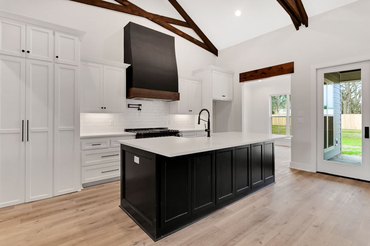 Kitchen with white cabinets, black island, vaulted ceiling with exposed beams, and modern range hood.