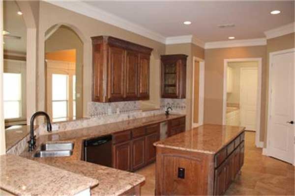 Kitchen with wood cabinets, granite countertops, double sink, island, and view through archway to dining area.
