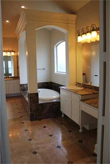 Bathroom with oval soaking tub, arched window, double vanity, and marble floor.
