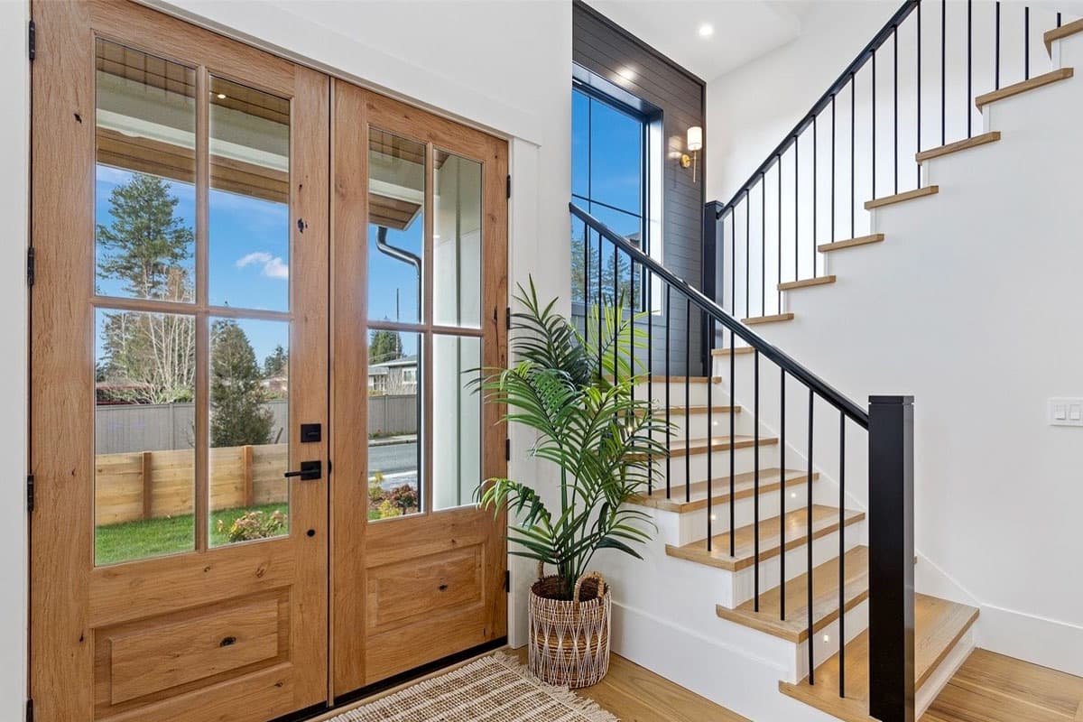 Modern staircase with wood treads and black metal balusters adjacent to double wood-paneled glass doors.