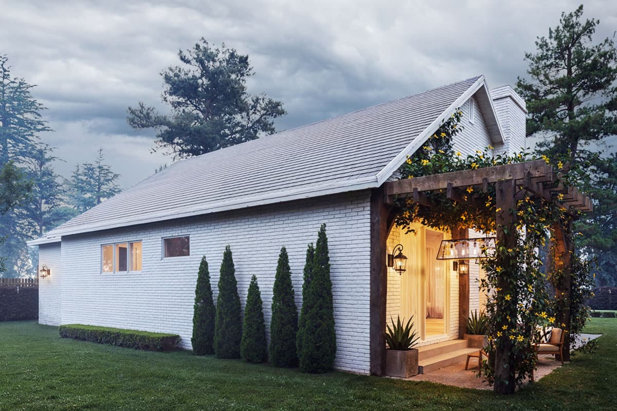 House plan exterior: white brick, gabled roof, covered pergola with climbing vines and interior lighting.