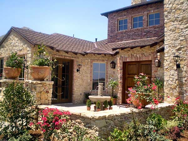House plan exterior with stone and brick facade, multiple gables, pitched roof, and wooden double doors.