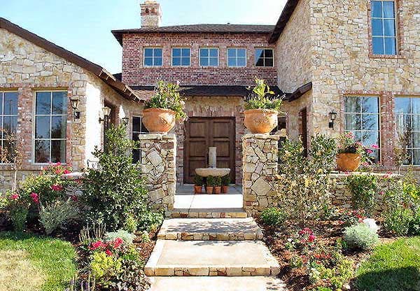 House plan exterior featuring stone and brick facade, double wooden doors, and tiered fountain.