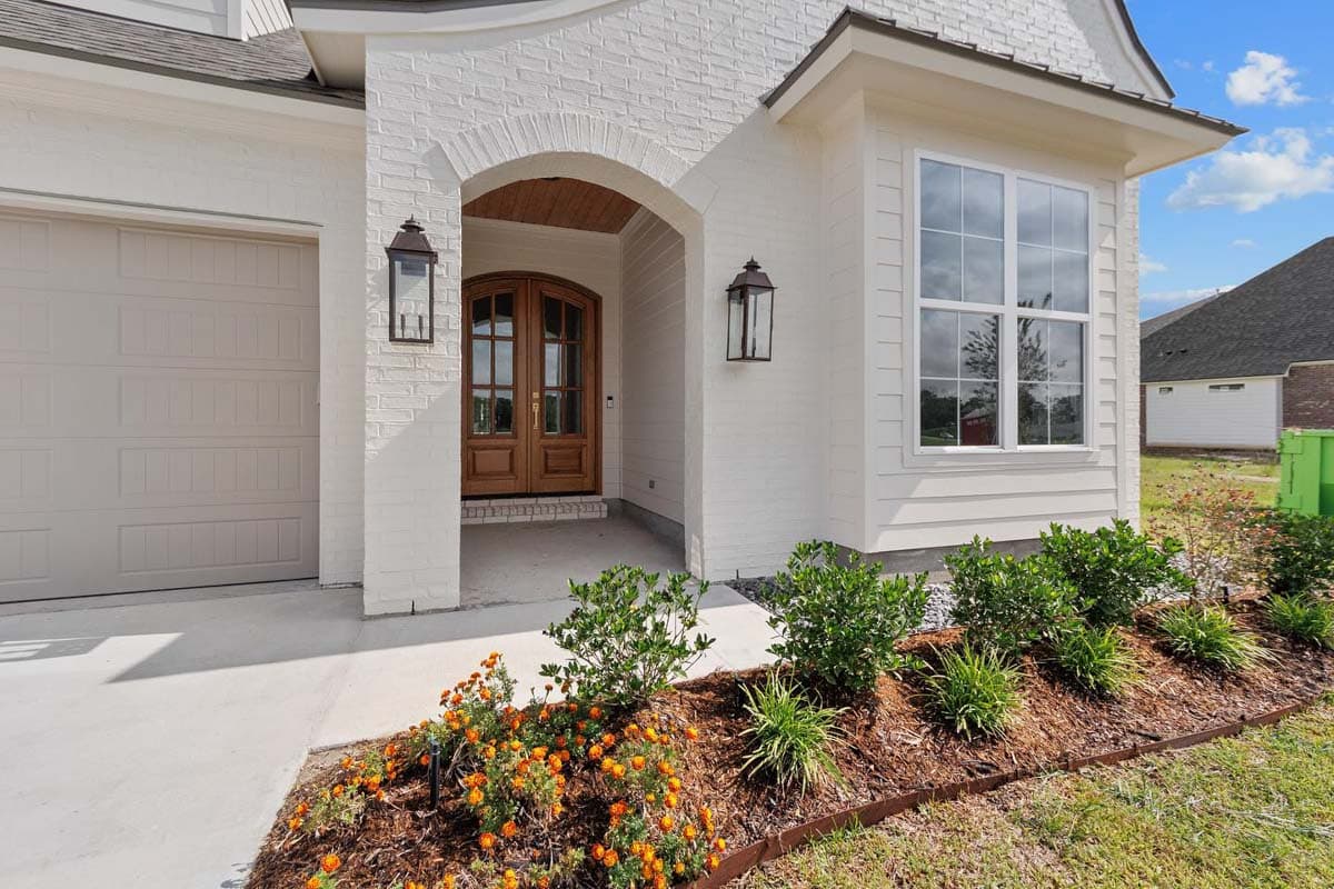 House plan exterior features arched entry with double wooden doors, white brick facade, garage, and a large window.