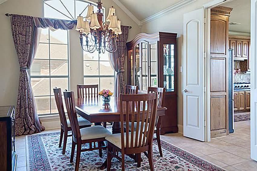 Dining room with wood table and chairs, vaulted ceiling, large arched window, china cabinet, and view into kitchen.