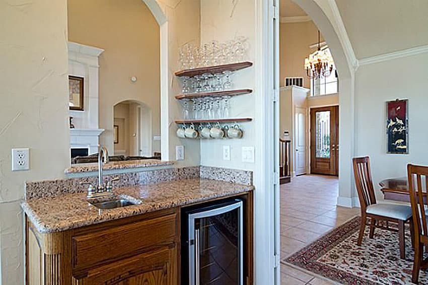 Wet bar with granite counter, sink, wine fridge, and hanging glass rack. Entry hall with chandelier and double doors visible.