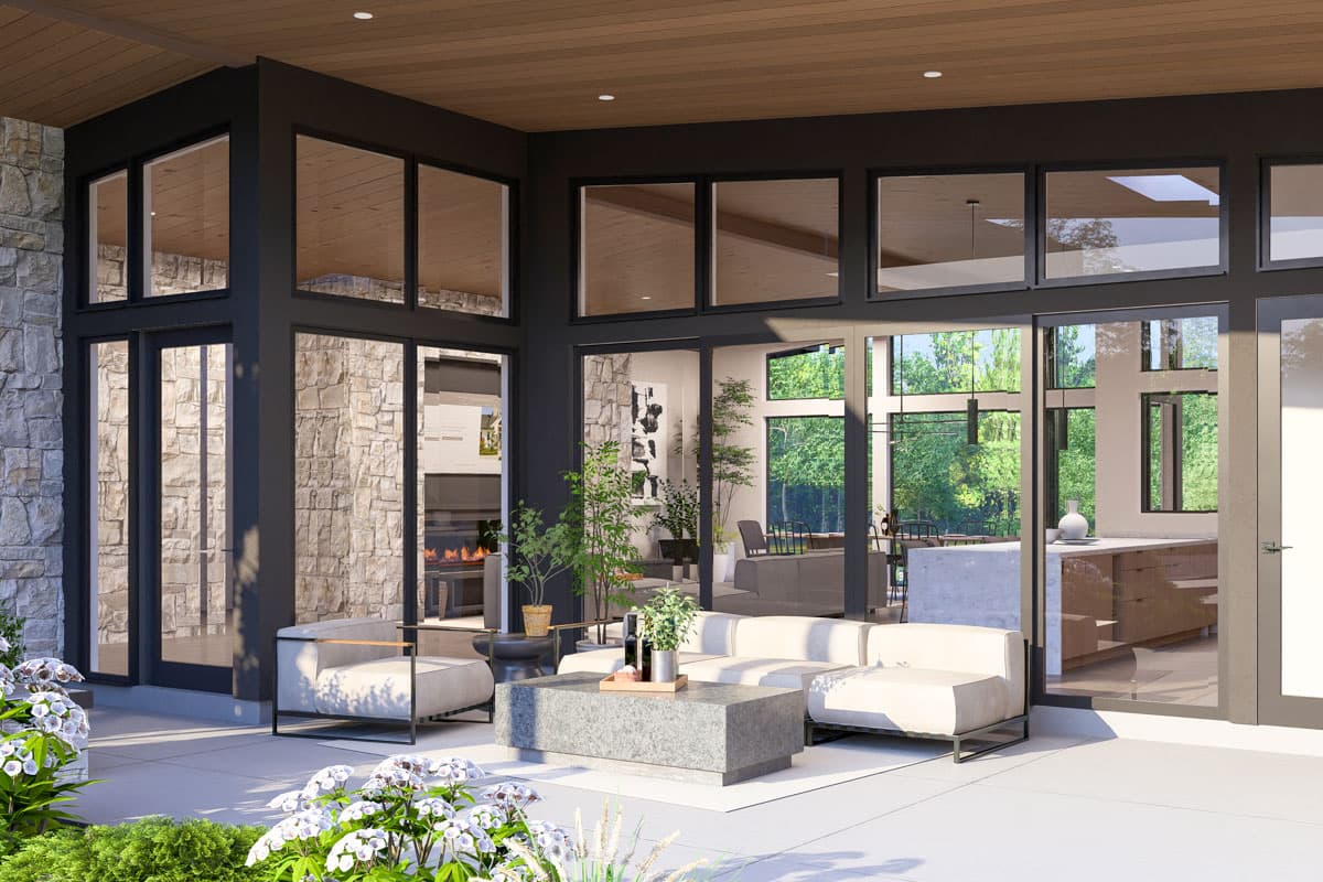 Modern house plan exterior with stone facade, large windows, and covered patio. Open-concept interior visible with fireplace and kitchen.