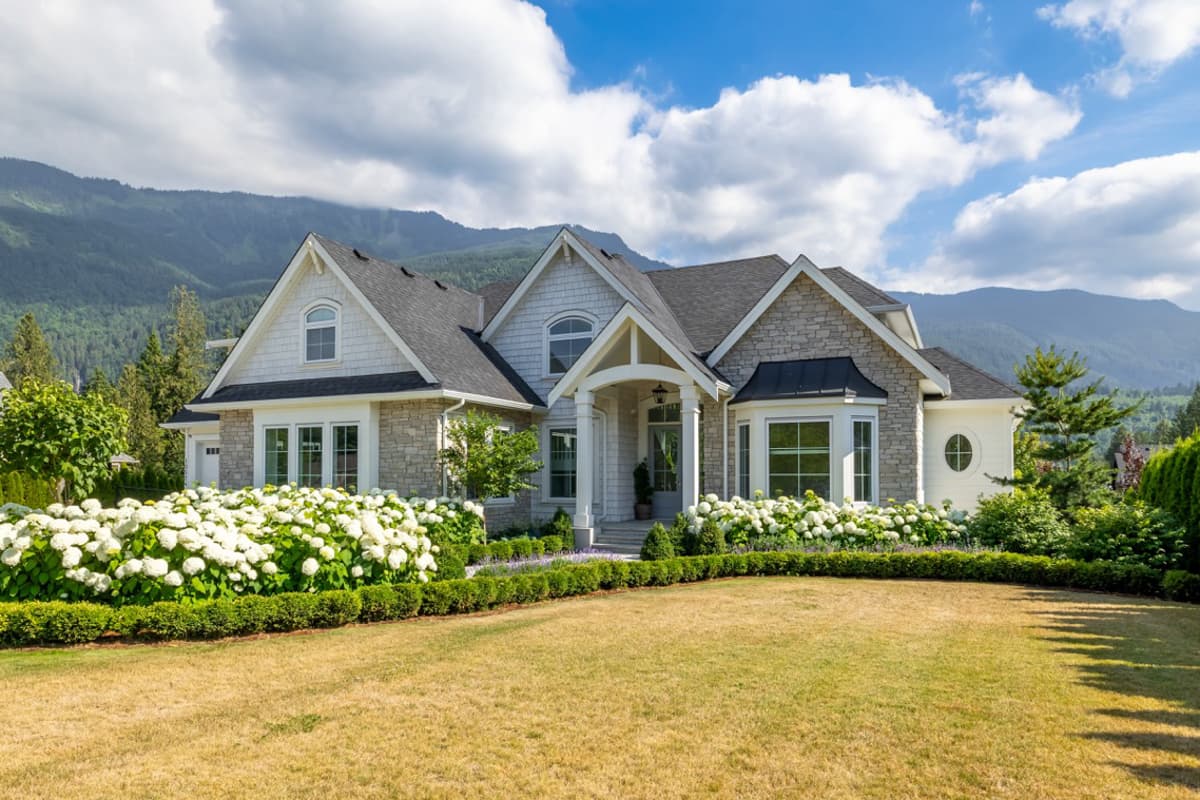 House plan exterior. Two-story home with stone accents, arched dormer window, and covered entry with columns. Features multiple gables and bay window.