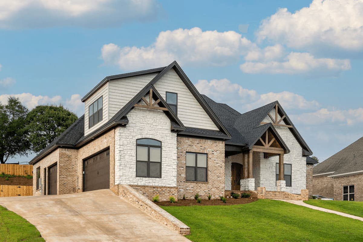 House plan exterior with stone and brick facade, gabled dormers, exposed wood beams, and a three-car garage.