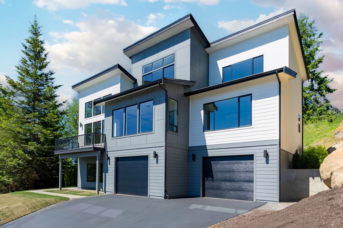 Modern house plan exterior with multiple gables, large windows, and a two-car garage. Balcony overlooks a sloped lawn.