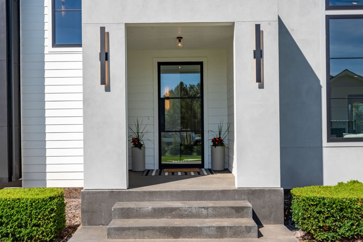 Modern house plan exterior featuring a covered entry, black-framed glass door, and geometric wall sconces.