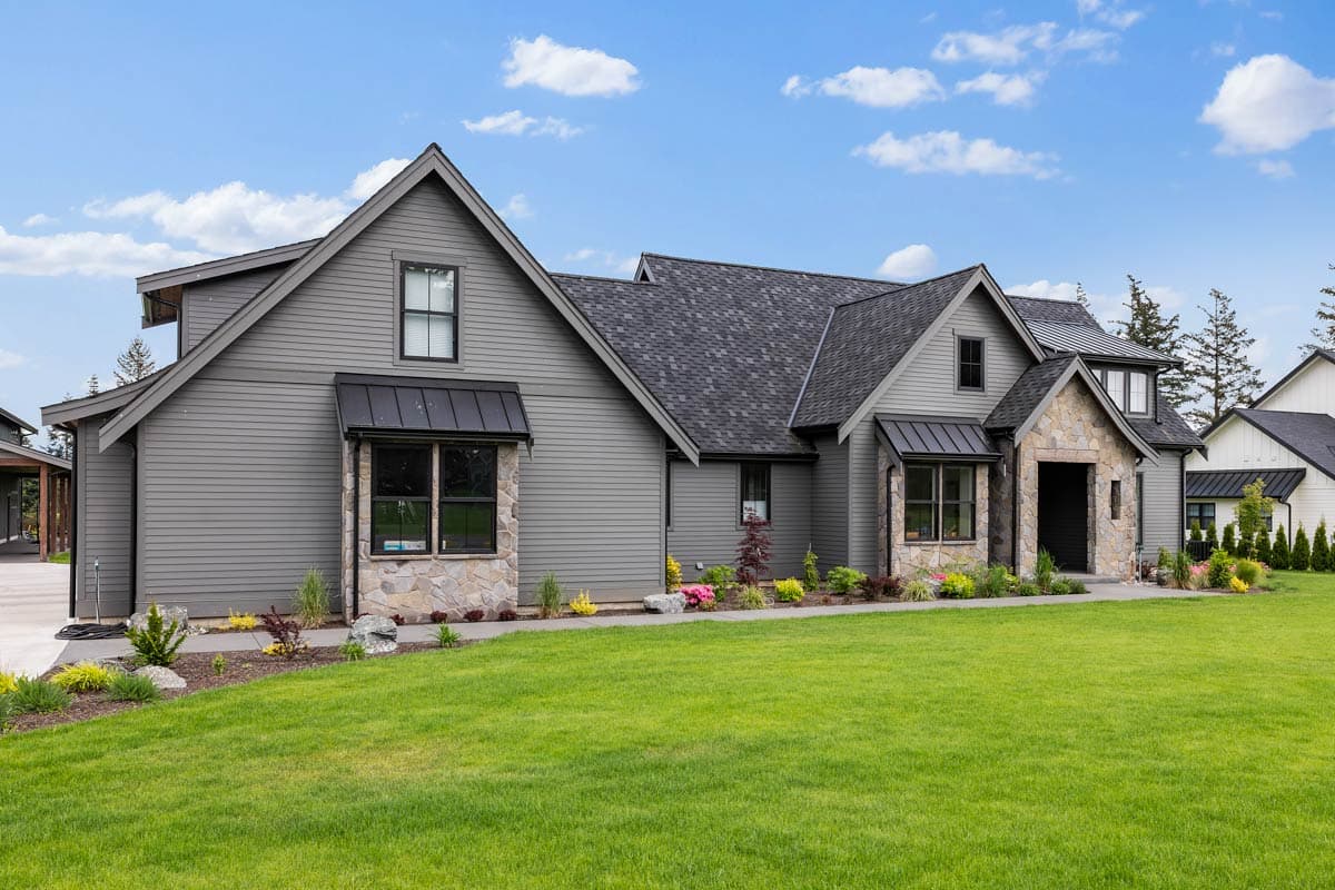 House plan exterior: Modern Farmhouse style, two stories, stone accents, prominent gables, dark metal awnings over windows.