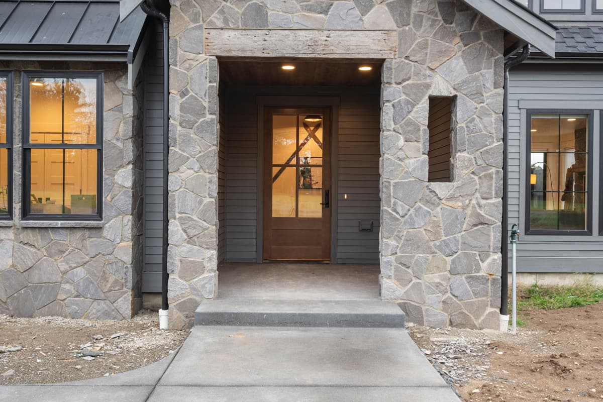 Exterior view of house plan featuring stone facade, covered entryway, and dark-trimmed windows.