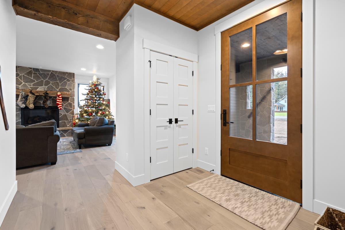 Interior view of modern house entrance with double doors, stone fireplace, and Christmas tree. Exposed wood beams and ceiling.