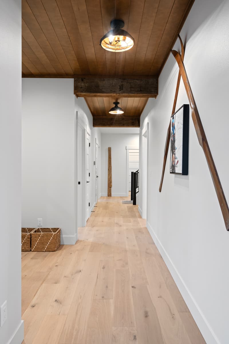 Hallway with wood plank ceiling, exposed beams, wood floors, and doors leading to rooms. Decorative oars on wall.
