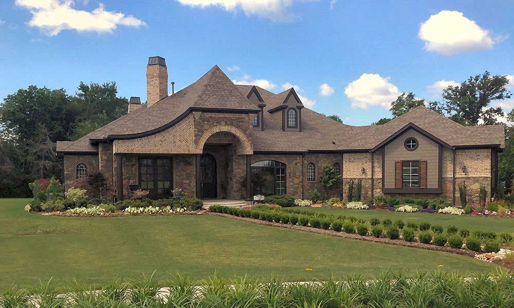 House plan exterior of a multi-story home with stone and brick facade, arched entry, multiple gables, and dormer windows.