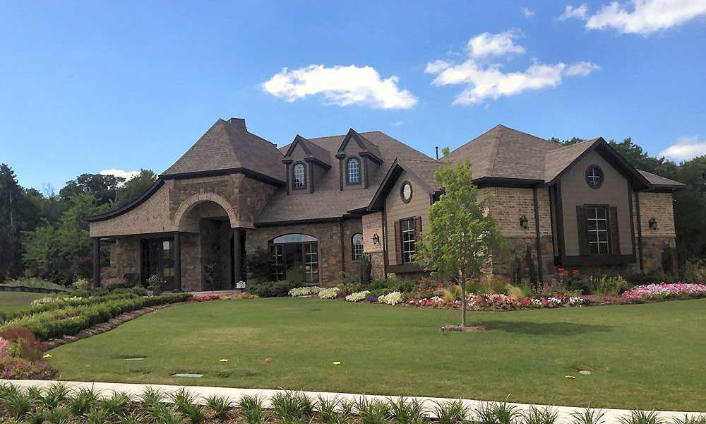 House plan exterior: Two-story home with stone and brick facade, arched entryway, multiple gables, and dormer windows.