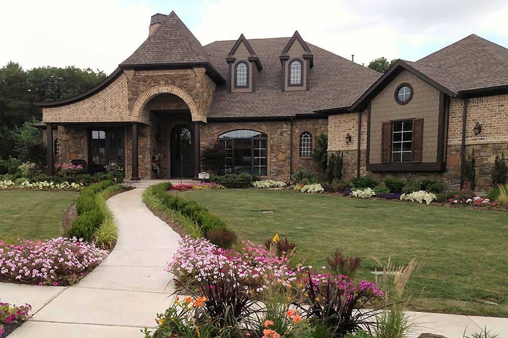 House plan exterior featuring stone and brick facade, arched entryway, multiple gables, and dormer windows.