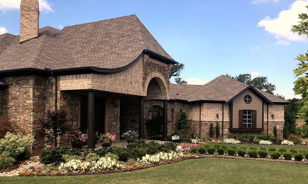 House plan exterior with stone and brick facade, arched entry, prominent chimney, and a gabled dormer.