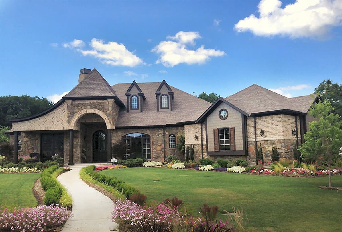 House plan exterior featuring stone and brick facade, arched entryway, multiple gables, and dormer windows.