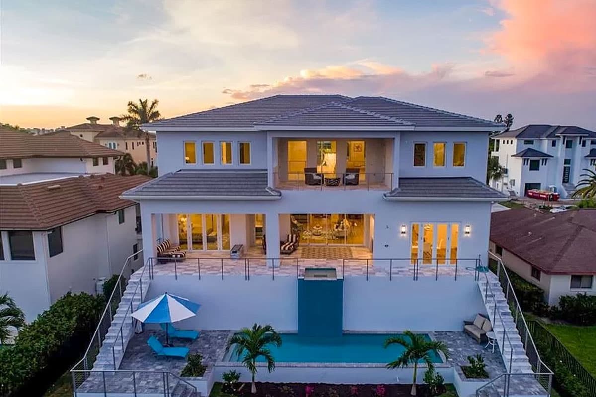 Two-story house plan exterior with multiple balconies, large windows, a tiled roof, and a swimming pool.