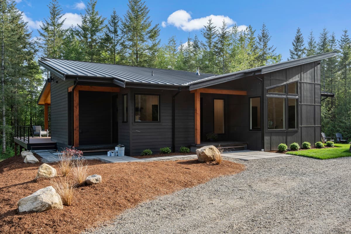 Modern house plan exterior with dark siding, angled rooflines, and exposed wood beams. Single story.