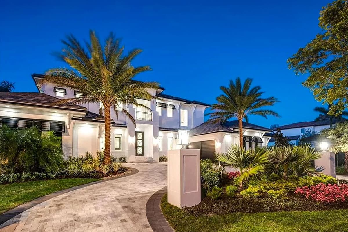 Modern two-story house exterior with a curved driveway, balcony, and expansive landscaping.