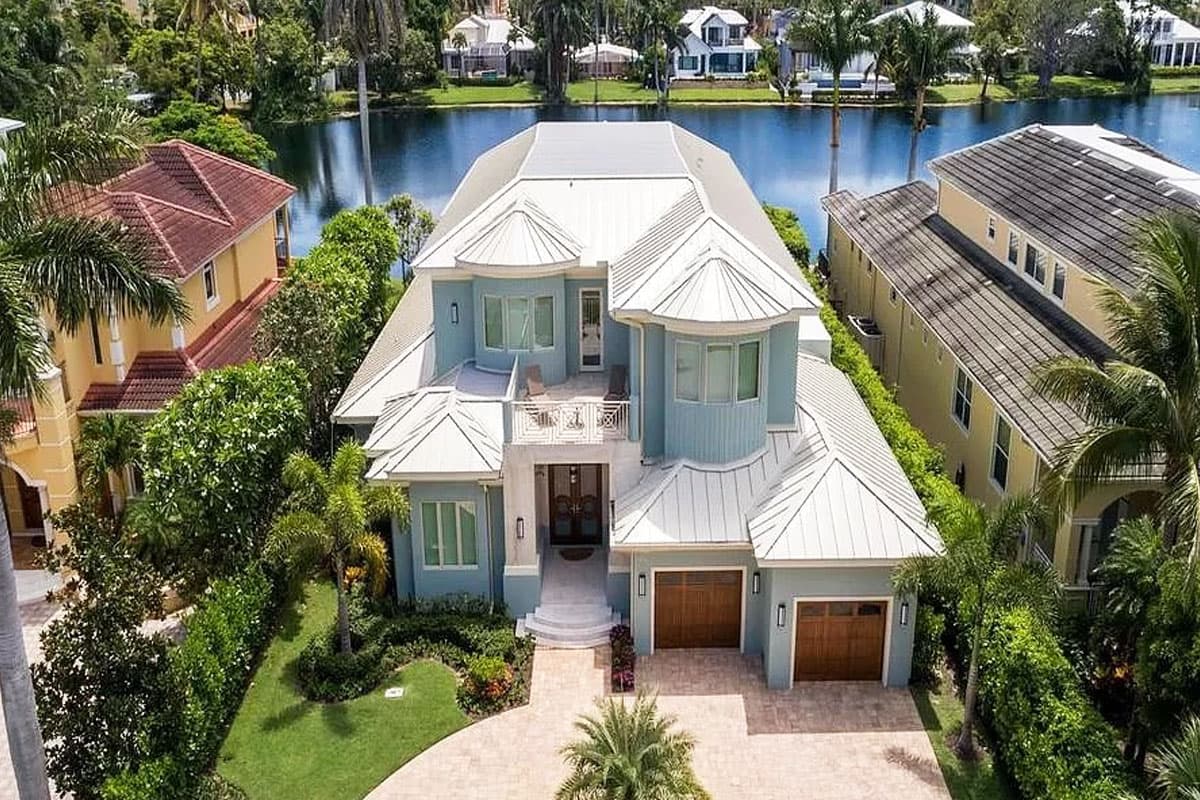House plan exterior view of a two-story home with a light blue facade, white metal roof, balconies, and a three-car garage.